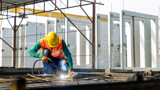 Worker at an infastructure manufacturing site welding cnc machined construction components.